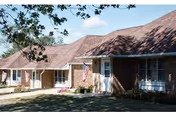Single-story Mayflower Community facility exterior with porch, flag, and shaded lawn.