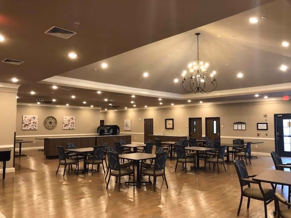 Spacious dining room with multiple tables and chairs, a serving counter, and a central chandelier.