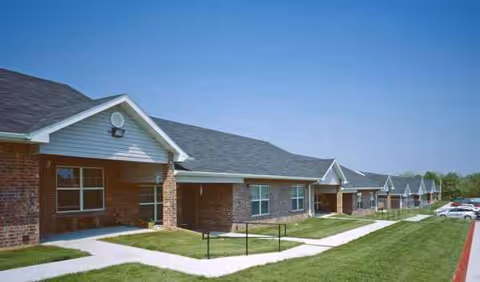 Row of single-story brick senior housing buildings with green lawn and walkway.