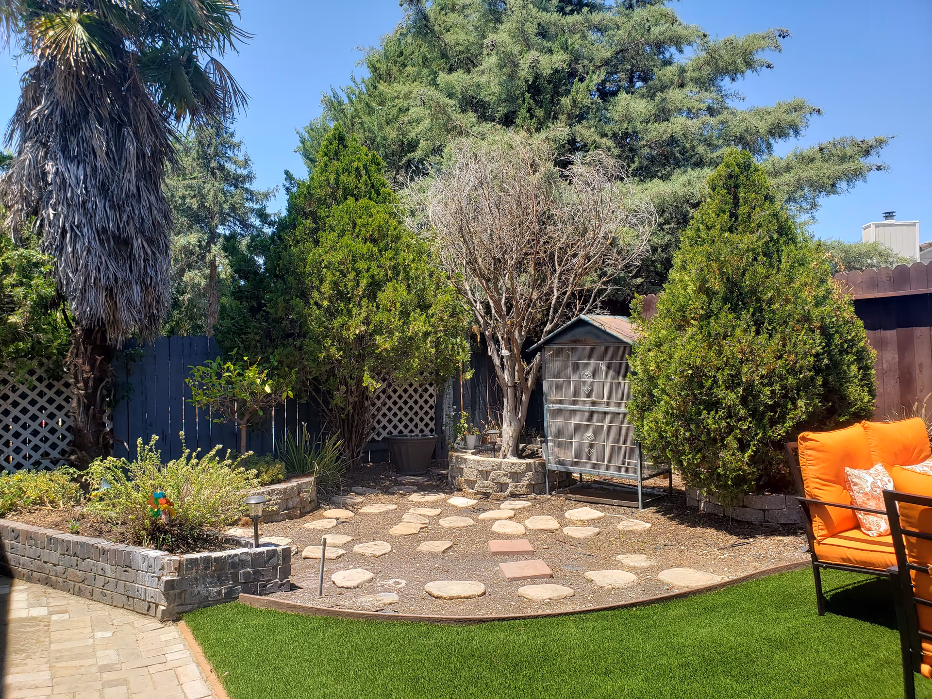 Backyard garden with stepping-stone path, trees, a small shed and orange patio chairs.