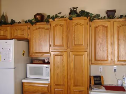 Wooden kitchen cabinets line the wall with a fridge, microwave, and greenery decor.