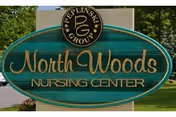 A green oval sign reading 'North Woods Nursing Center' with a Peplinski Group logo, displayed outdoors with trees in the background.