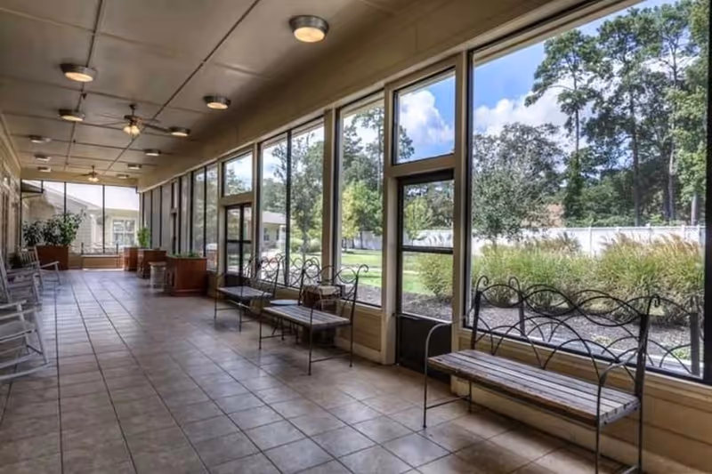 Bright enclosed sunroom with tiled floor, metal benches and large floor-to-ceiling windows overlooking a landscaped courtyard.