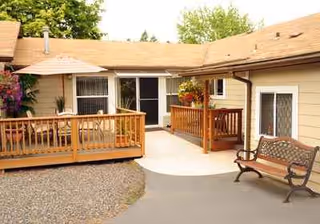 Exterior view of Ana's AFCH senior living courtyard with a wooden deck, bench, and umbrella.