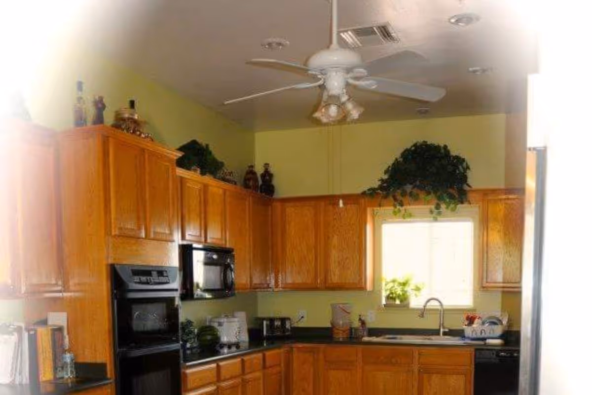 Well-lit kitchen with oak cabinets, a ceiling fan, built-in oven and microwave, and a sink under a window.