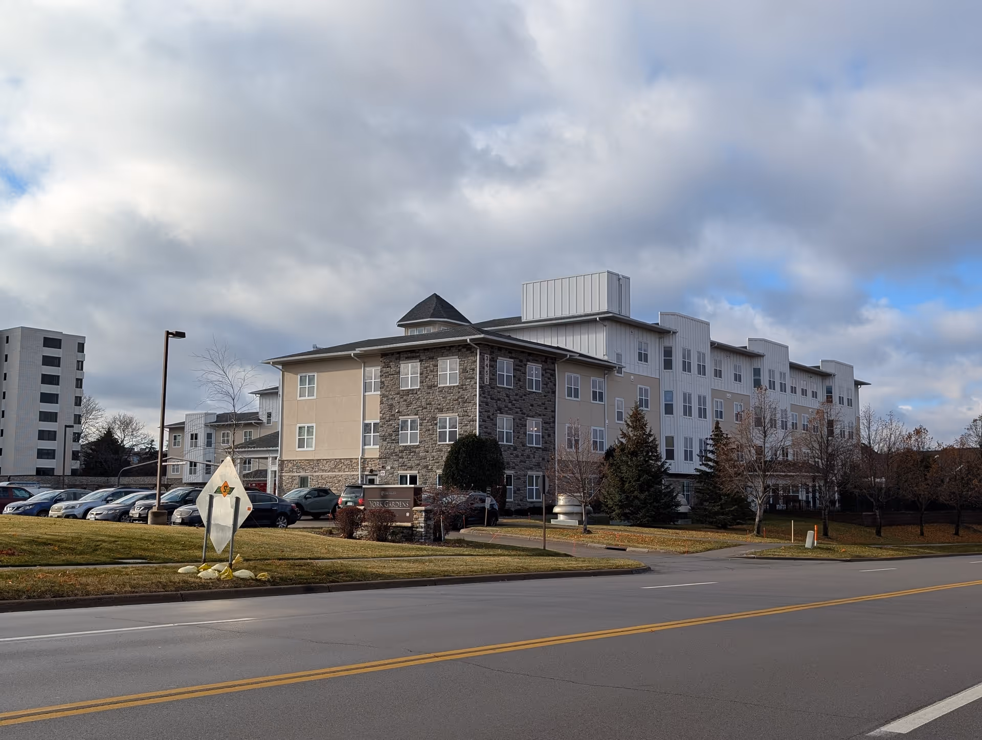 Street view of the York Gardens multi-story senior living building with parked cars and a cloudy sky.