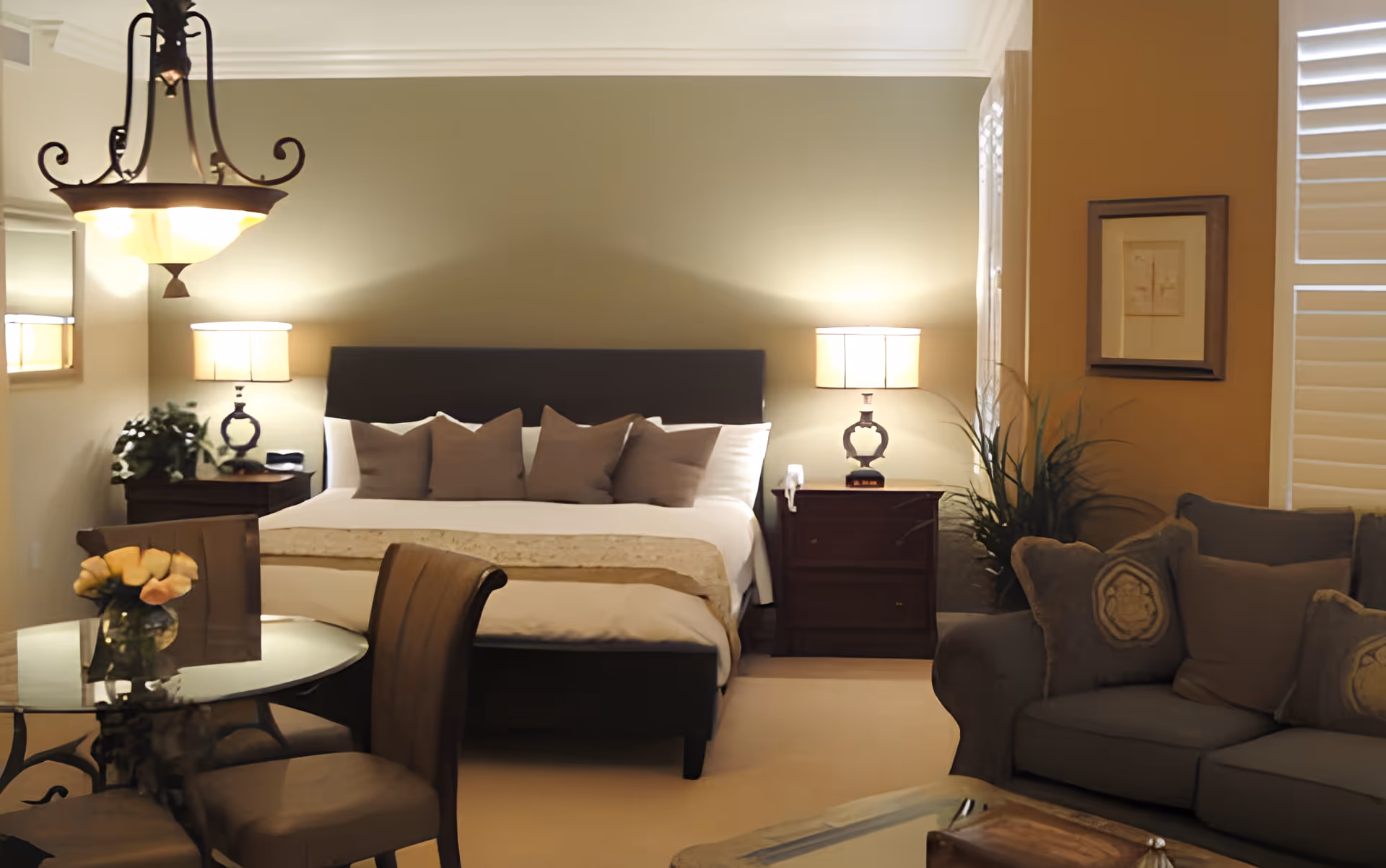 Well-lit bedroom with a king-size bed, bedside lamps, a sitting area and a small dining table.