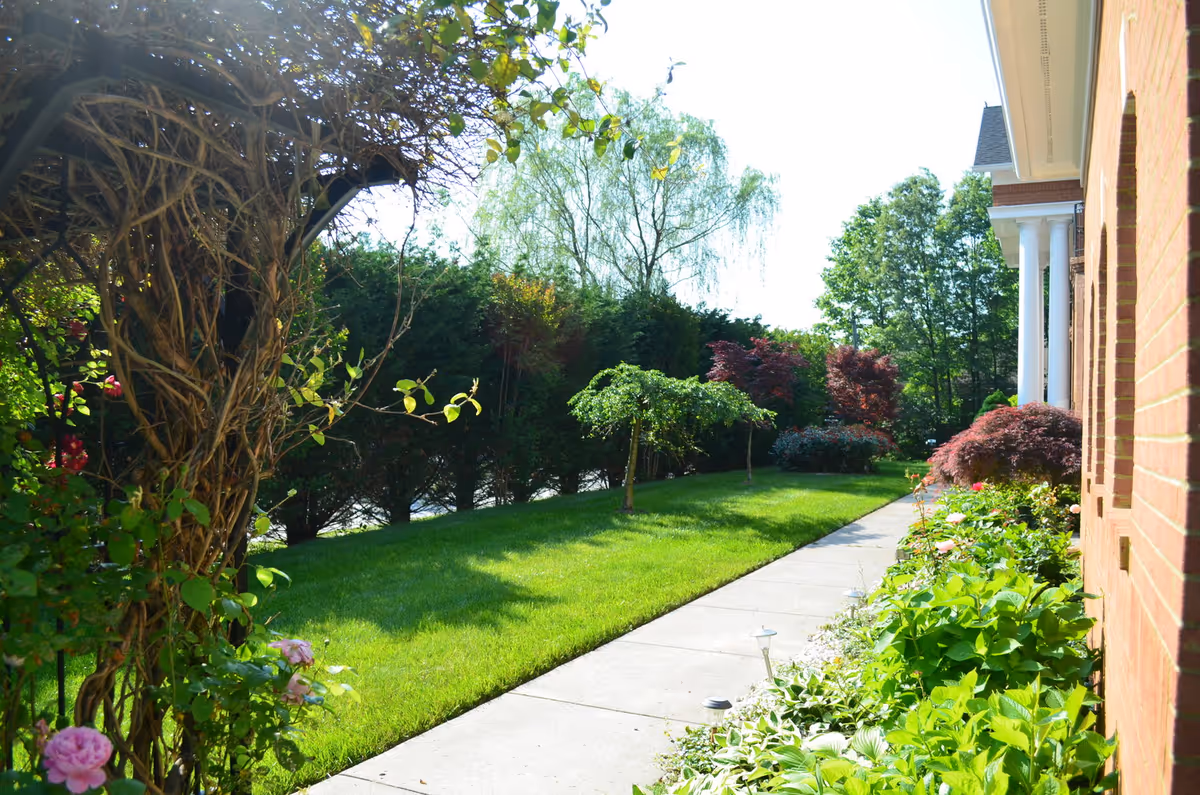 Brick building along a concrete walkway with a manicured lawn and lush garden.