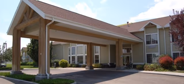 Exterior view of Brookdale Twin Falls senior living facility showing the front entrance with a large covered drop-off area supported by wooden beams, surrounded by landscaping and a clear sky.
