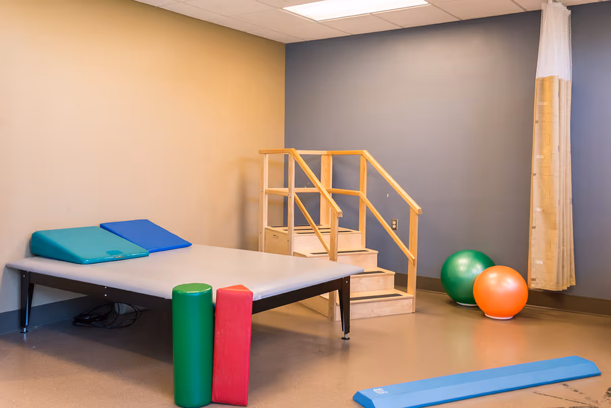 Physical therapy room with a low padded treatment table, wooden practice stairs, exercise balls and foam supports.
