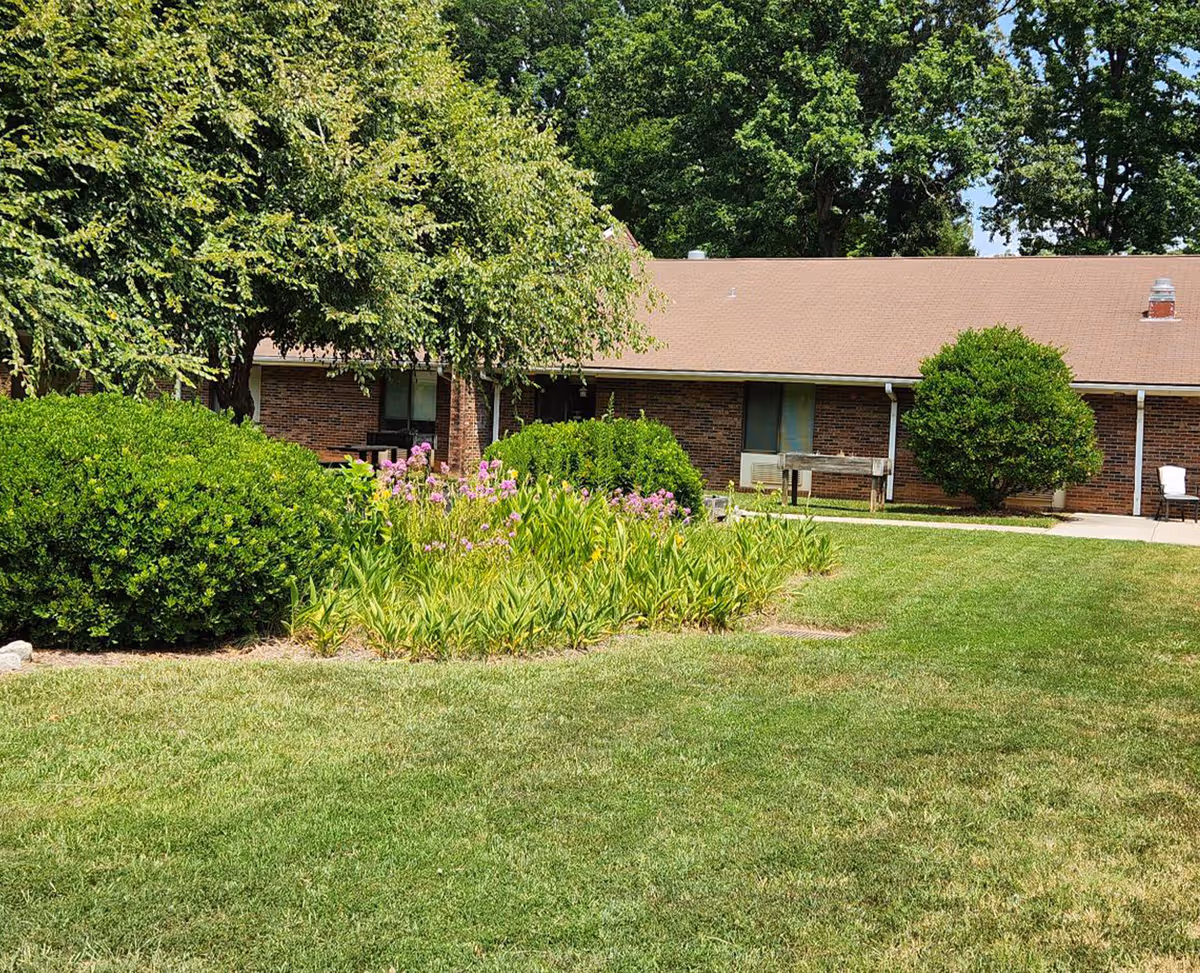 Brick single-story facility with manicured lawn, trees, and a bench along the entrance.