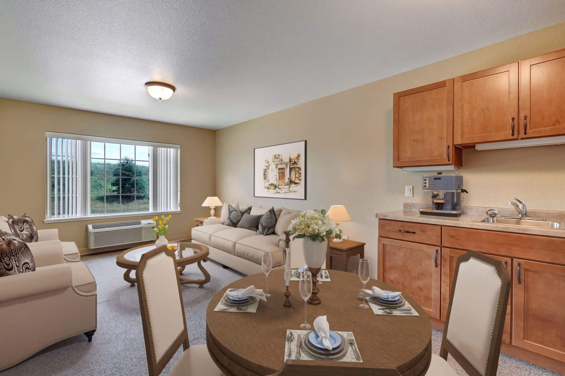 A cozy senior living room and kitchenette area featuring a beige sofa with decorative pillows, two matching armchairs, a round wooden dining table set with plates, napkins, and glasses, wooden cabinets with a sink and coffee machine, a large window with vertical blinds, and soft lighting from ceiling and table lamps.