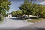 Exterior view of Azalea Manor campus with trees, parked cars, and a driveway.