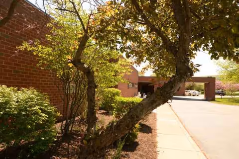 Brick senior living facility with trees, a sidewalk, and a driveway at the entrance.
