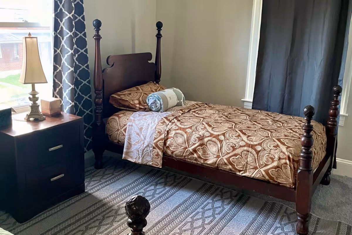 Dark wood four-poster bed with patterned bedding sits in a cozy bedroom.