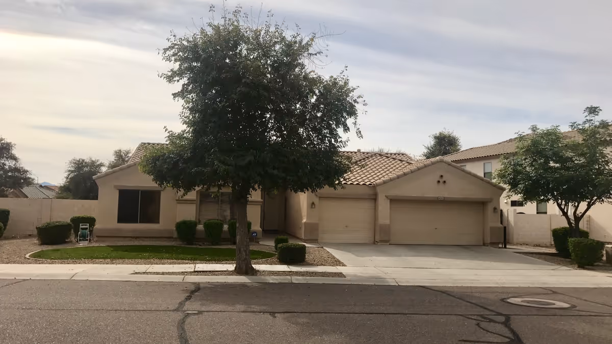 Single-story suburban house with a three-car garage, front lawn, and a tree in the driveway.