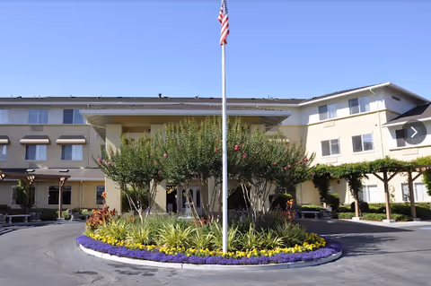 Exterior view of Carlton Senior Living San Jose with landscaped roundabout and flagpole.