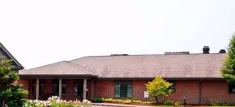 Front view of a single-story brick senior living building with shrubs and a small tree.