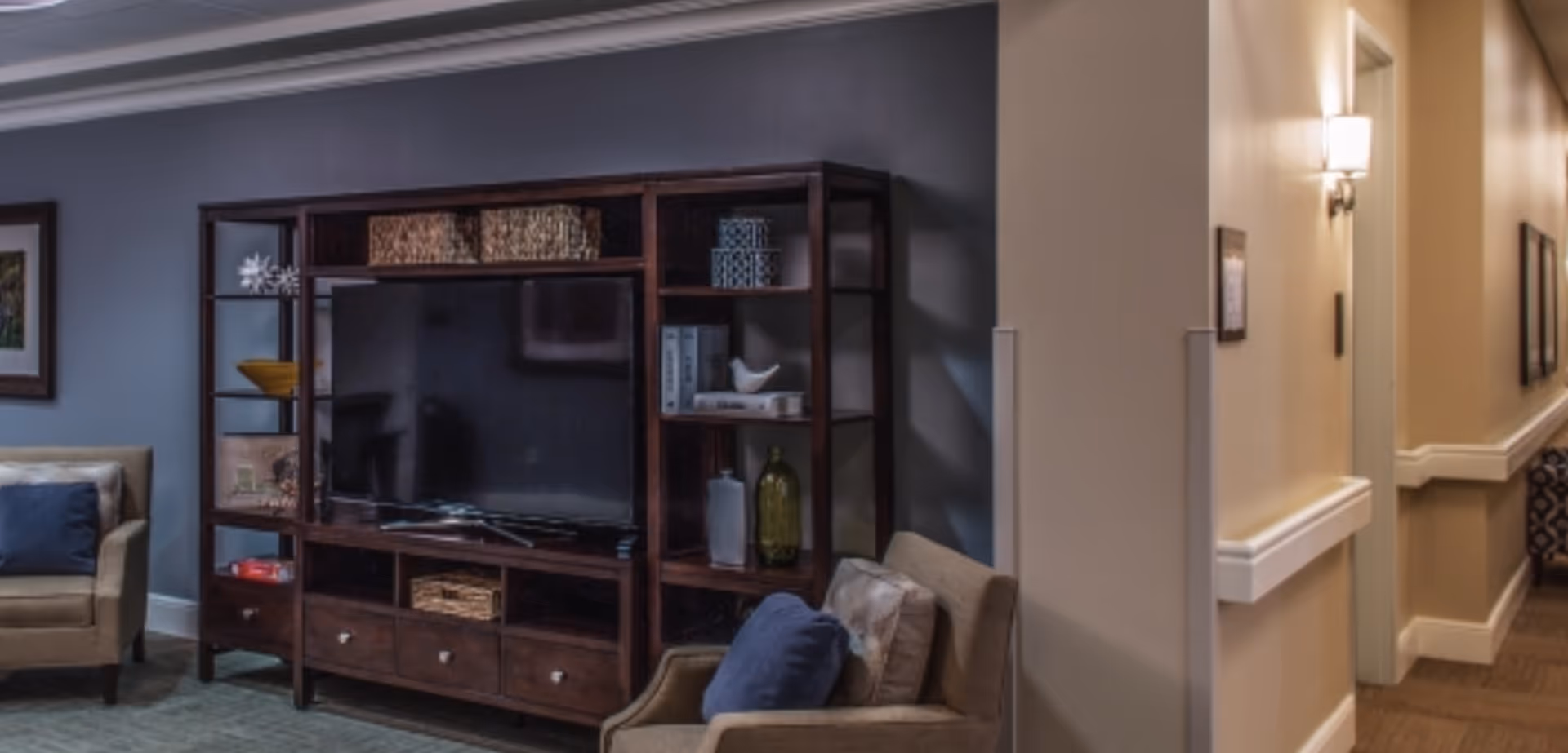 Cozy living room with a large wooden TV shelving unit, armchairs, and a hallway to the right.