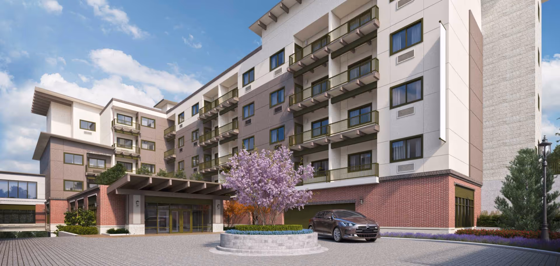 Exterior view of a multi-story assisted living building with an entrance canopy, a parked car, and a flowering tree in a circular planter.