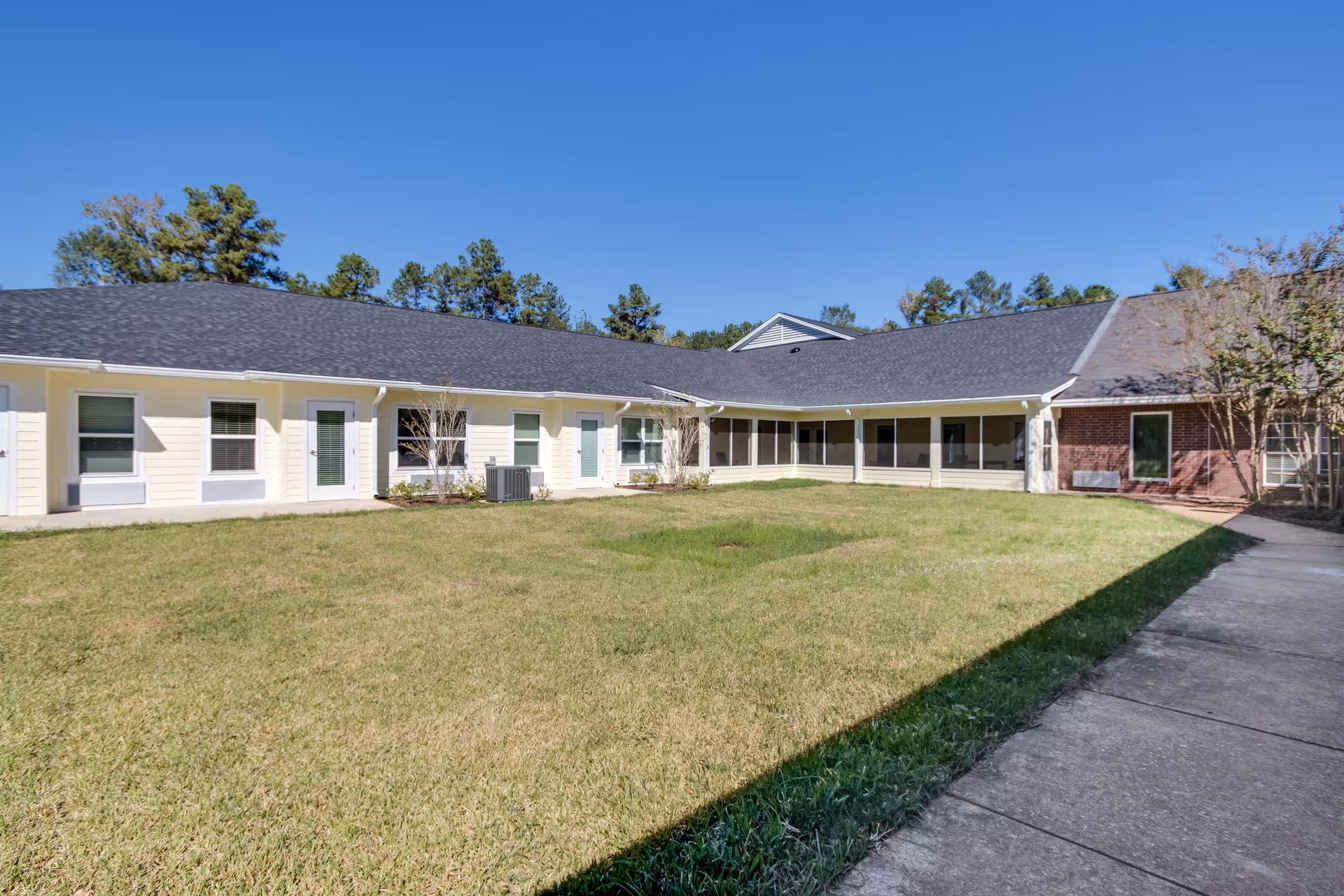Sunny central courtyard with a lawn surrounded by a single-story assisted living building under a clear blue sky.