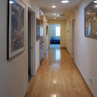 Bright hallway in a senior living facility with wooden floors and framed artwork.