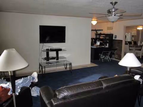 Living room in a senior facility with TV, sofa, lamps, and ceiling fan.