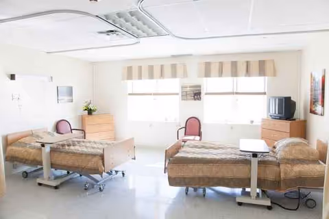 Two hospital beds and chairs in a bright shared room at Beach Terrace Care Center