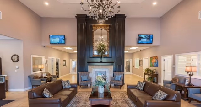 Spacious lounge with leather sofas facing a central coffee table and a fireplace with a large mirror under a chandelier.