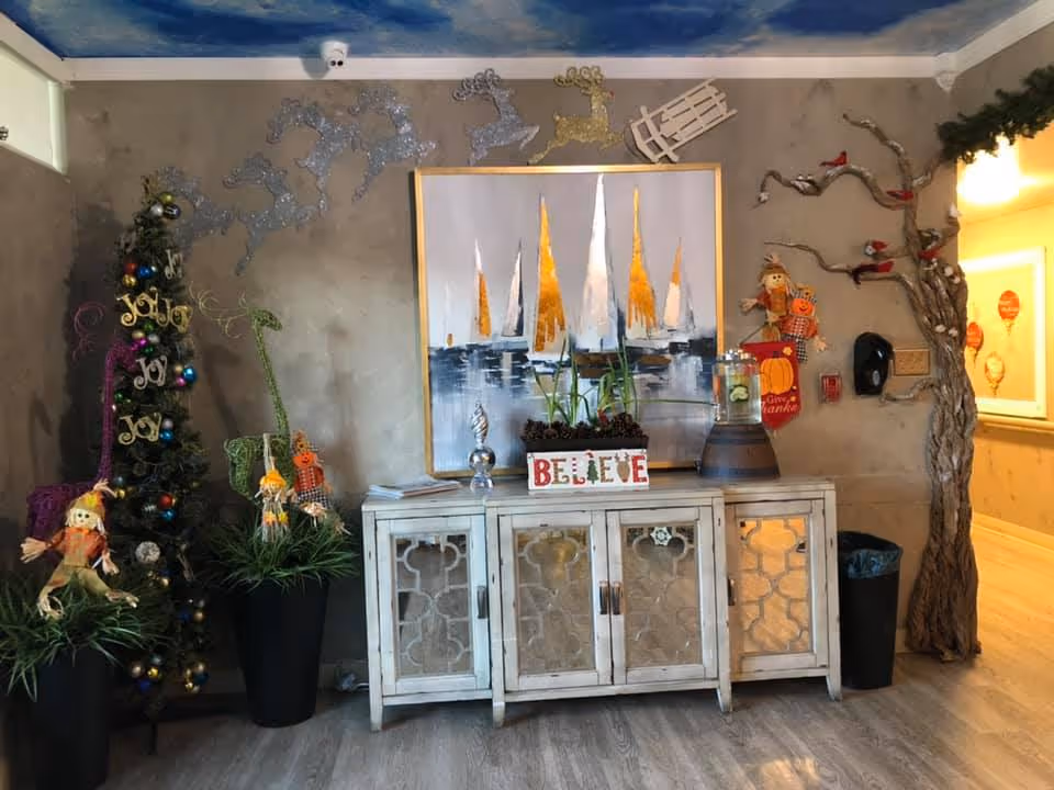 Decorated common-area console with a sailboat painting, a 'BELIEVE' sign, holiday decorations and a small Christmas tree.