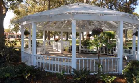 White gazebo with seating in a landscaped outdoor area at Natchitoches Nursing & Rehab.