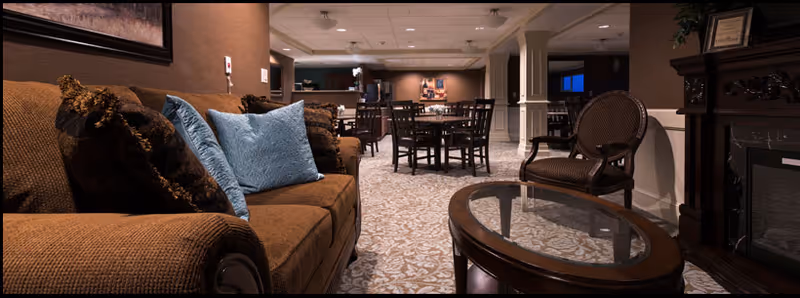 Interior communal lounge area with a brown sofa, glass-top coffee table, dining chairs and a fireplace.