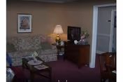 Cozy living room with a floral sofa, coffee and side tables, lamp, TV cabinet, and framed artwork.