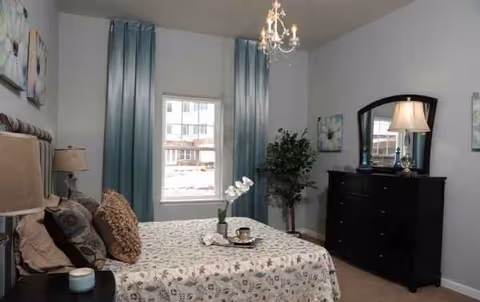 Bedroom at Arbour Square of Harleysville with bed, dresser, chandelier.