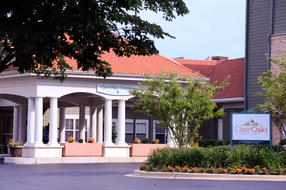 Front entrance of a senior living community with white columns, landscaping, and a Clare Oaks sign.