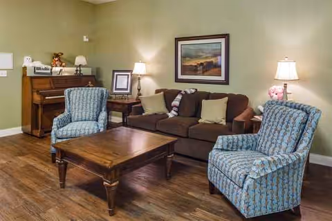 A cozy living room with seating, a coffee table, piano, and framed artwork.