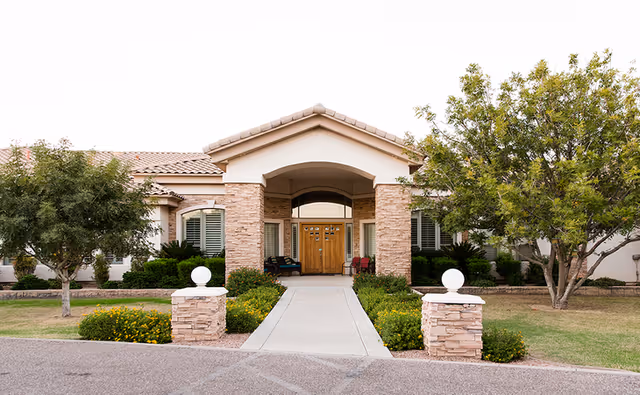Front entrance of Emerald Groves senior living facility with brick columns and landscaped walkway.