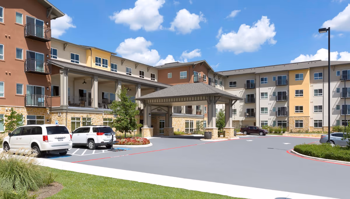 Exterior front of a multi-story senior living building with a covered entrance, balconies, and parked cars.