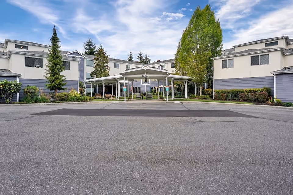 Front exterior view of Mountlake Terrace Plaza, showing a multi-story building with a covered entrance and surrounding greenery under a partly cloudy sky.