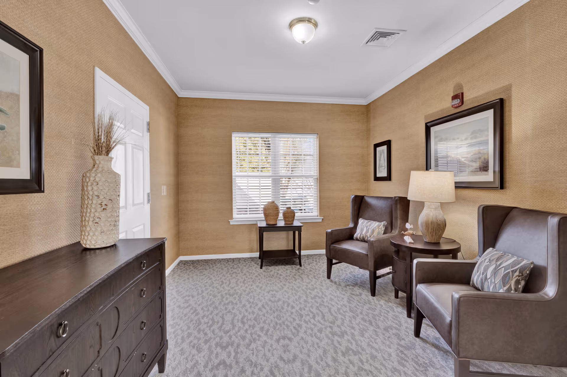 A cozy sitting room with two leather armchairs, a side table and lamp, a dresser, window, and decorative accents.