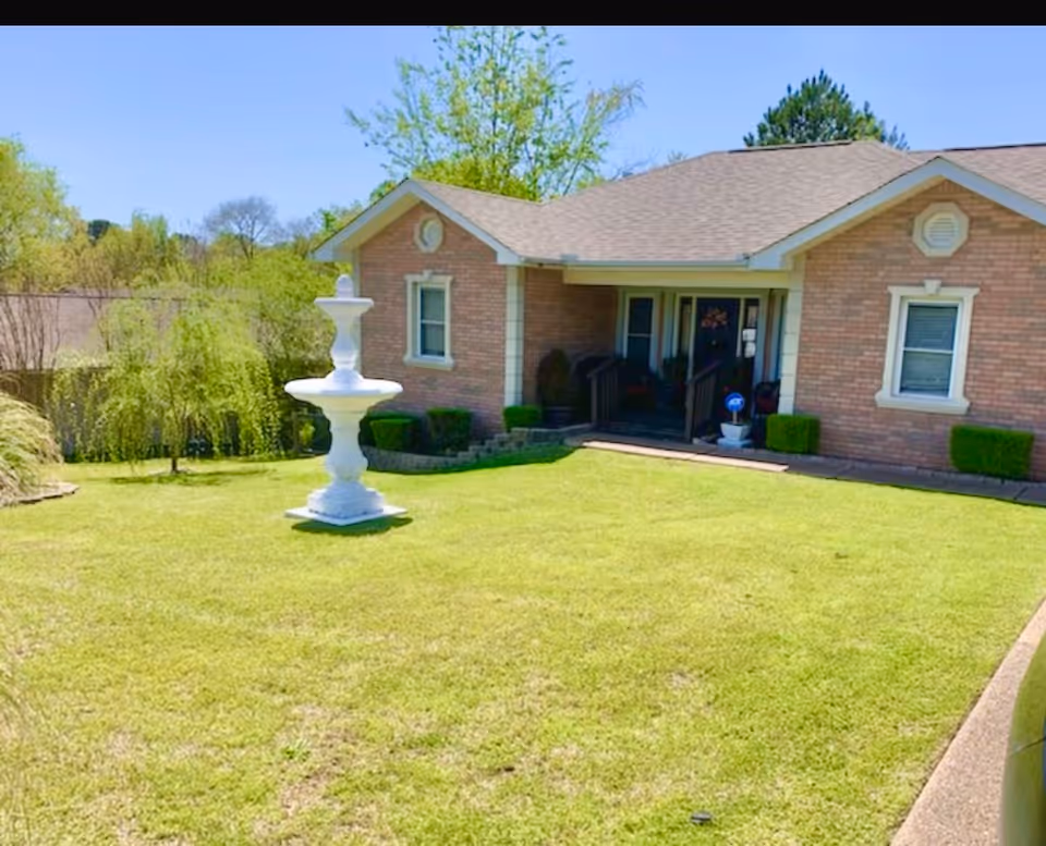 Brick one-story building with front steps, green lawn, and a tall white fountain.