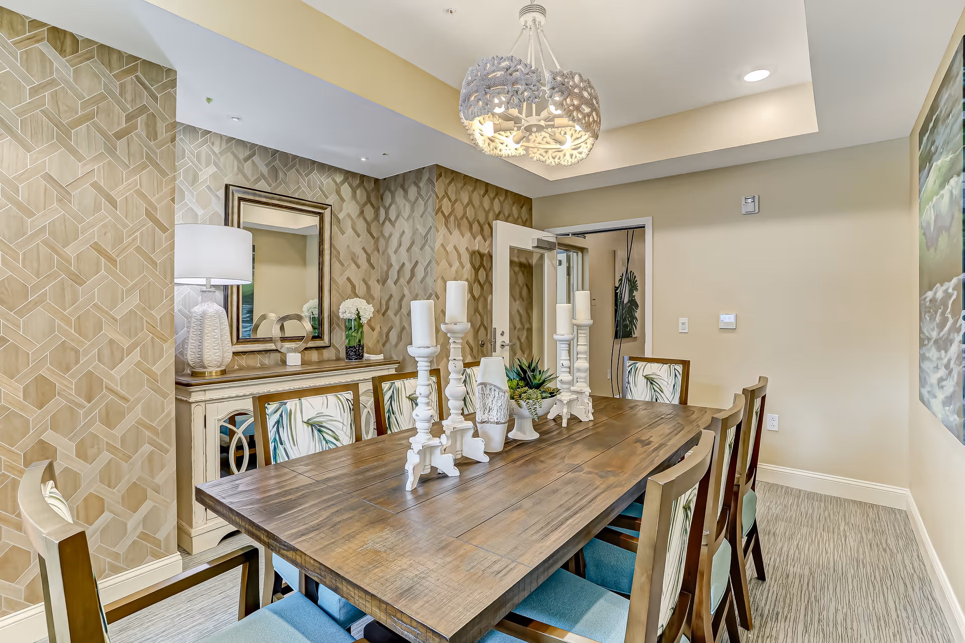 A well-decorated dining room with a long wooden table, chairs, decorative candles and a sideboard against patterned wallpaper.