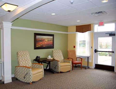 Lounge area with green walls, two patterned armchairs, a small table, and an exit door.