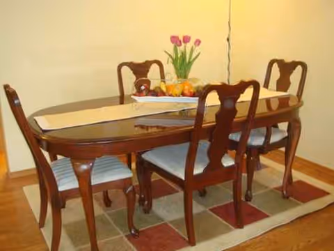 Wooden dining table with six chairs, fruit centerpiece, in a cozy dining room.