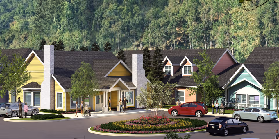 Colorful cottage-style senior living community buildings with a circular flowerbed, parked cars, and people in front.