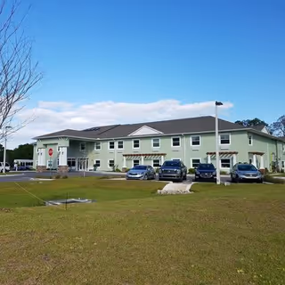 Exterior view of a two-story light green senior living facility building named Lake House with several parked cars in front and a clear blue sky above.