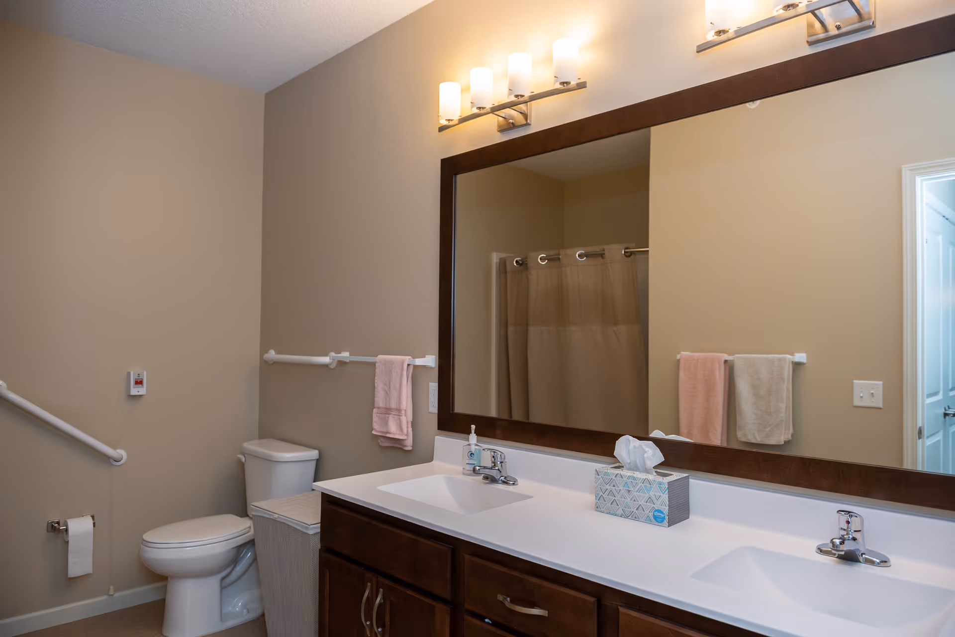 Accessible bathroom with a double-sink vanity, large mirror, toilet, grab bars, and towels.