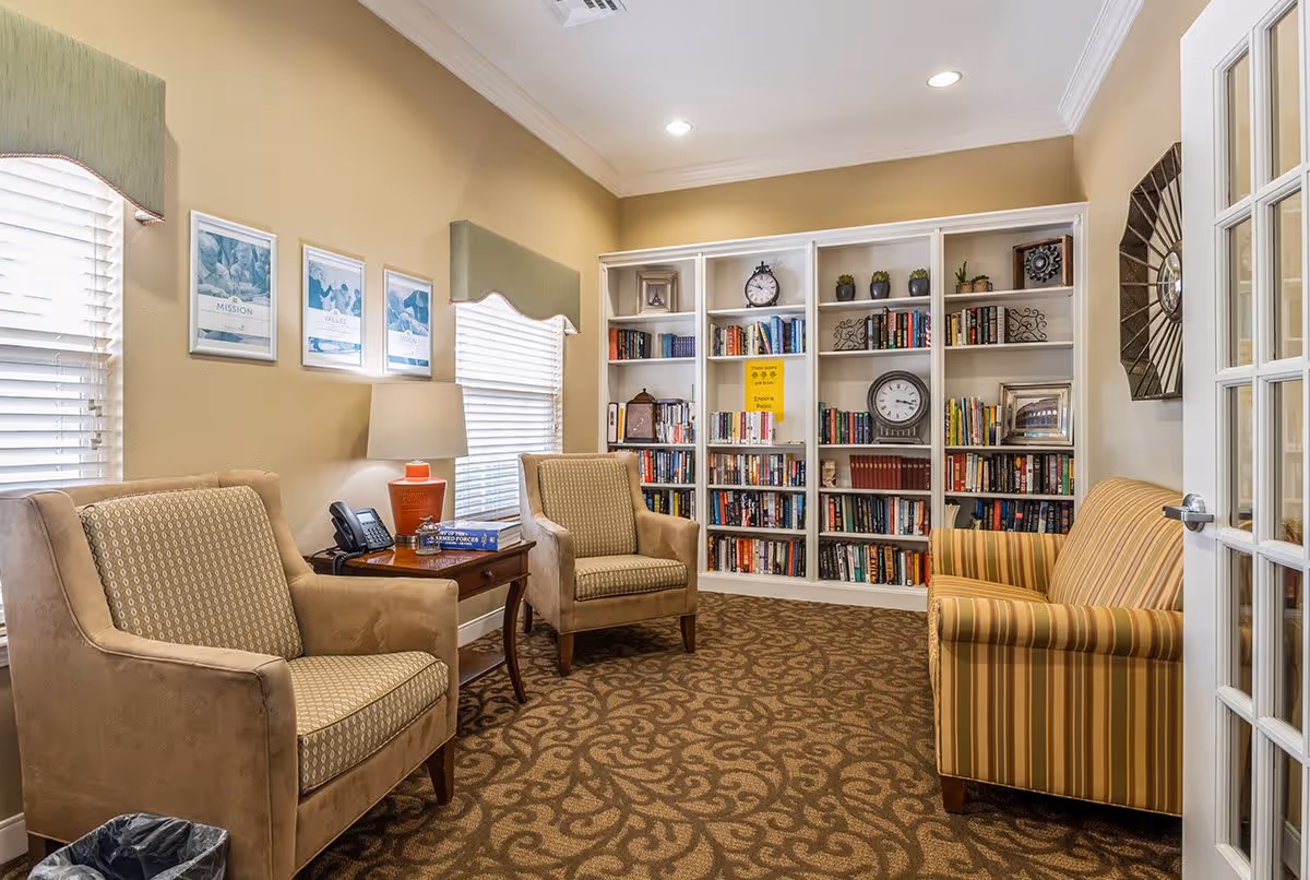Cozy sitting room with armchairs, a striped sofa, side table and a large bookshelf filled with books and clocks.