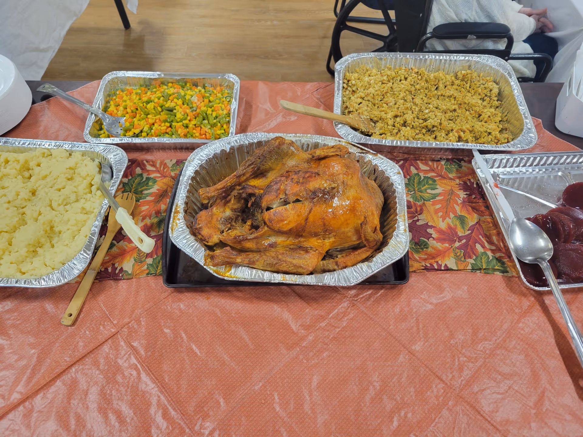 Buffet table with a roasted turkey in an aluminum pan surrounded by mashed potatoes, stuffing, mixed vegetables and cranberry sauce.