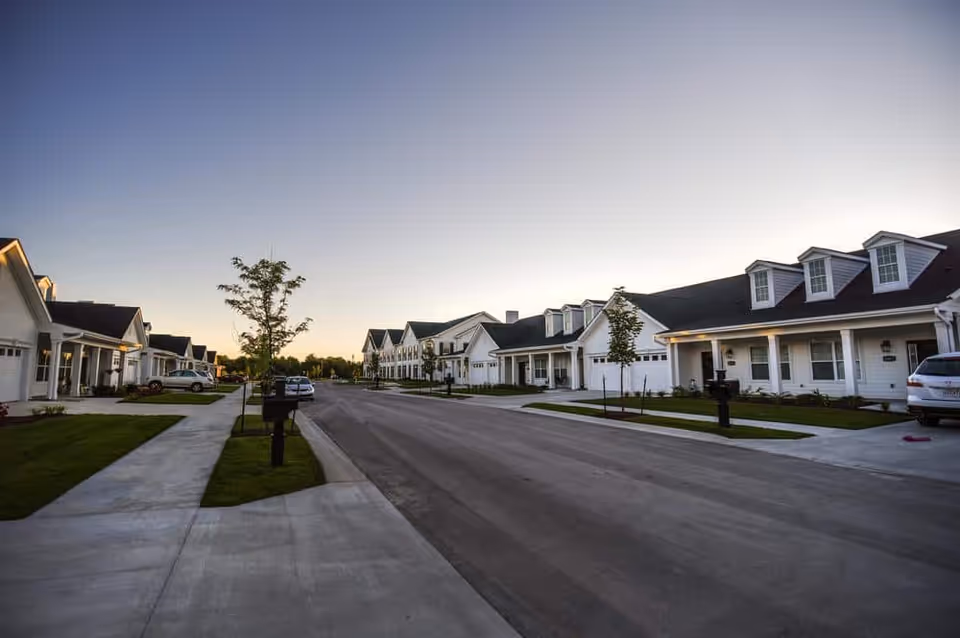 Row of white single-story residences with porches lining a quiet street at dusk.